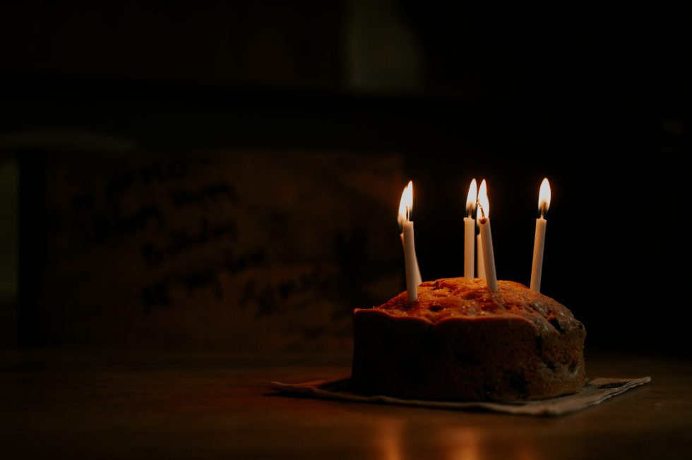 Chocolate birthday cake with four lit candles in dim lighting